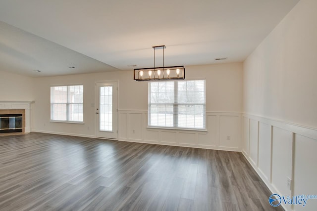 interior space with a decorative wall, a wainscoted wall, wood finished floors, visible vents, and a tiled fireplace