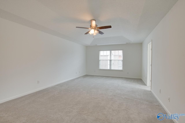 unfurnished room featuring baseboards, a raised ceiling, a ceiling fan, light colored carpet, and a textured ceiling