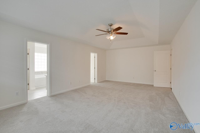 empty room featuring a raised ceiling, light colored carpet, ceiling fan, and baseboards