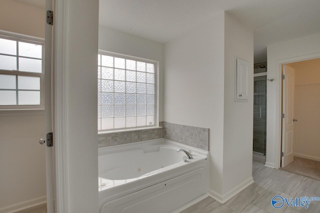 bathroom featuring baseboards, a jetted tub, and a stall shower