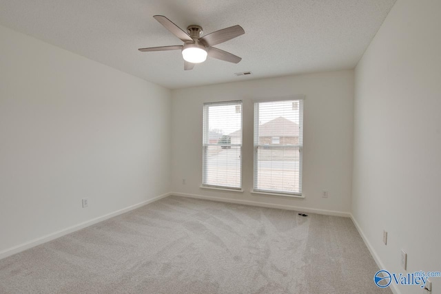 spare room with visible vents, baseboards, a ceiling fan, light colored carpet, and a textured ceiling