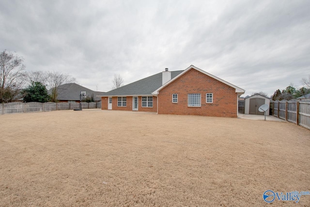 back of property with a fenced backyard, brick siding, an outdoor structure, a shed, and a chimney