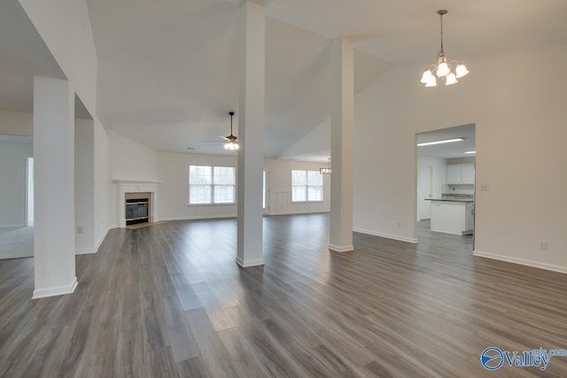 unfurnished living room with high vaulted ceiling, ceiling fan with notable chandelier, wood finished floors, baseboards, and a glass covered fireplace