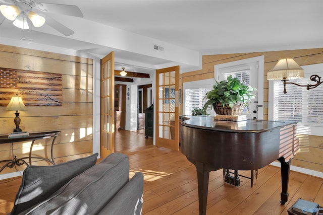 living area featuring visible vents, ceiling fan, wood walls, light wood-style flooring, and french doors