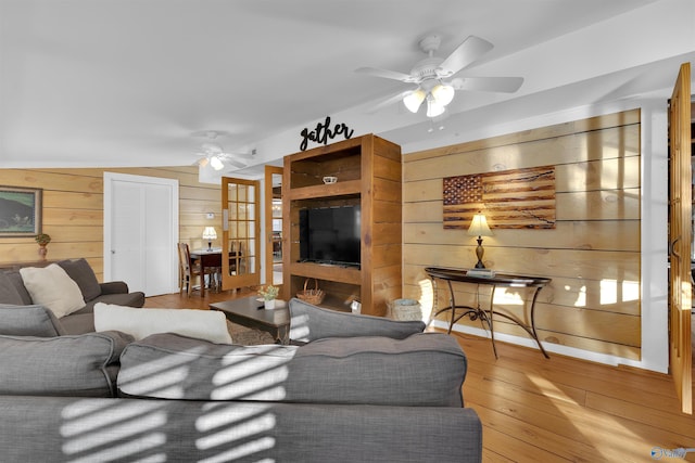 living room with wood walls, a ceiling fan, and hardwood / wood-style flooring