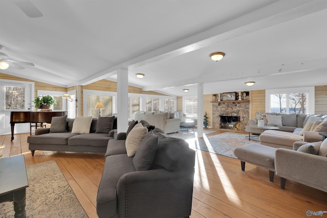 living room with a stone fireplace, light wood-type flooring, lofted ceiling with beams, and ceiling fan