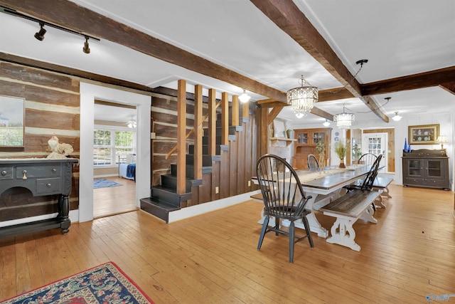 dining space featuring beam ceiling, wood-type flooring, wooden walls, an inviting chandelier, and stairs