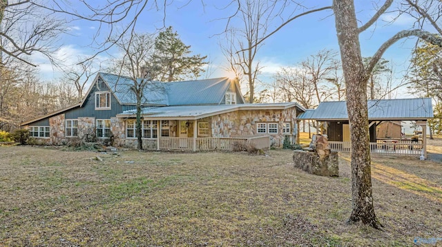 rear view of house featuring a porch, a lawn, stone siding, and metal roof