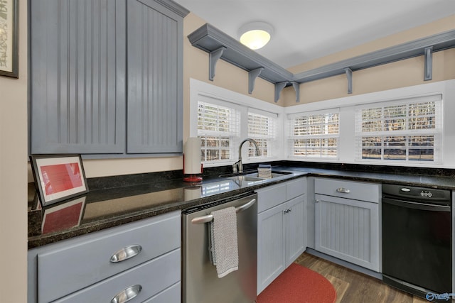 kitchen featuring dark stone counters, gray cabinets, stainless steel dishwasher, dark wood-style floors, and a sink