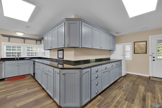 kitchen with gray cabinets, a skylight, dark wood-type flooring, and stainless steel dishwasher