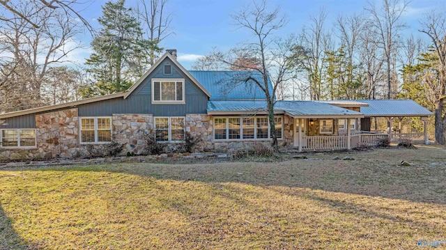 rear view of house featuring a lawn, covered porch, a chimney, metal roof, and stone siding