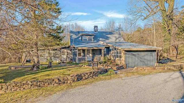 view of front of property with covered porch, a chimney, a front lawn, and metal roof