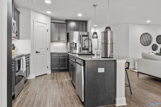 132 Fall Meadow Dr, Harvest, AL 35749 - kitchen with stainless steel appliances, wood finished floors, a center island with sink, a kitchen breakfast bar, and light stone countertops