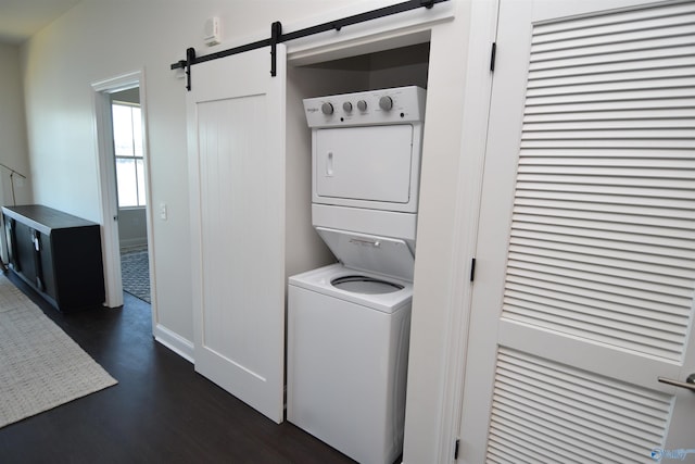clothes washing area with stacked washer and dryer, a barn door, laundry area, and dark wood finished floors