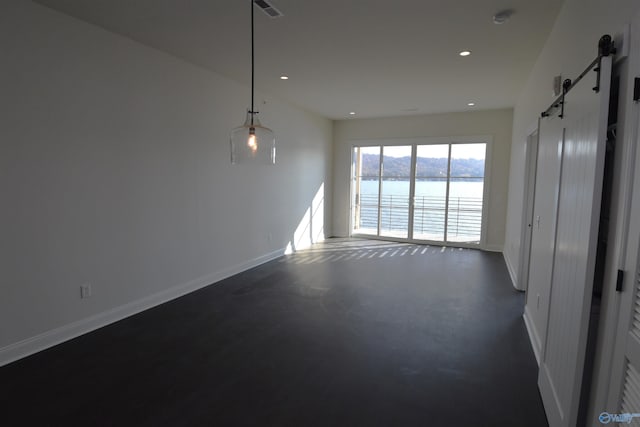 unfurnished room featuring a water view, recessed lighting, a barn door, and concrete flooring