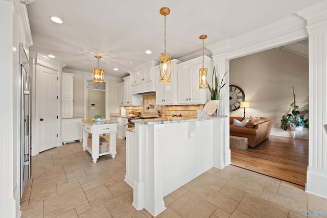 kitchen with white cabinetry, light stone counters, decorative light fixtures, kitchen peninsula, and backsplash