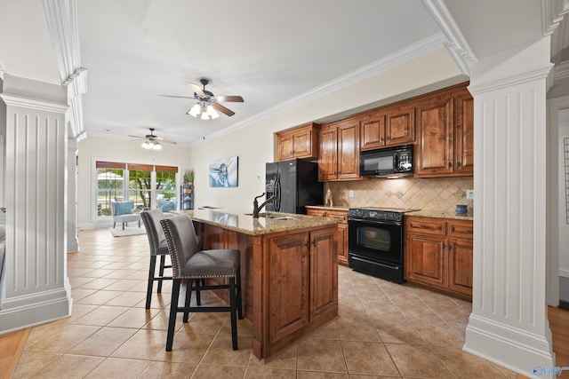 kitchen featuring light stone counters, light tile patterned floors, a kitchen breakfast bar, an island with sink, and black appliances