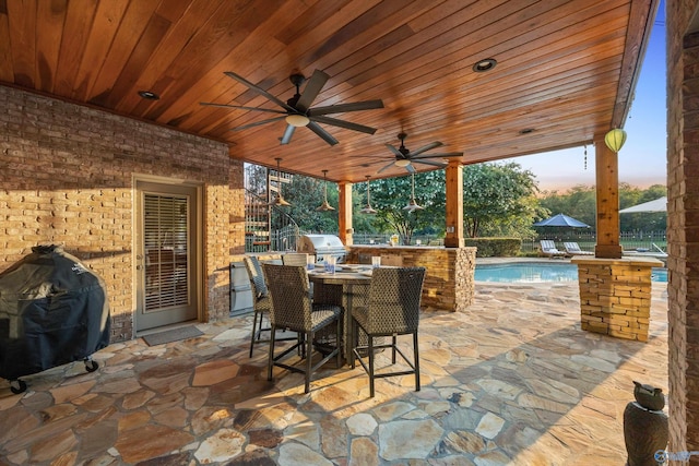 patio terrace at dusk with an outdoor kitchen, a grill, and ceiling fan