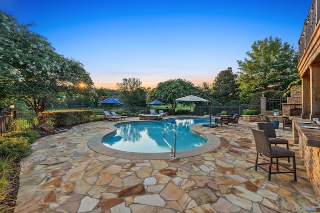 pool at dusk featuring a patio and a fireplace