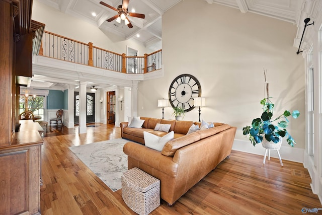 living room featuring coffered ceiling, decorative columns, light hardwood / wood-style flooring, a towering ceiling, and ceiling fan with notable chandelier