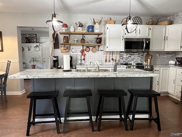 kitchen with a sink, stainless steel microwave, decorative backsplash, and white cabinets