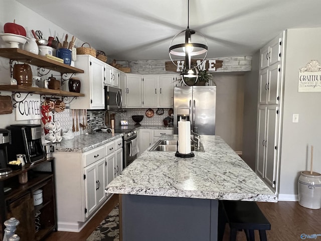 kitchen featuring a kitchen island with sink, a sink, appliances with stainless steel finishes, decorative backsplash, and dark wood-style floors