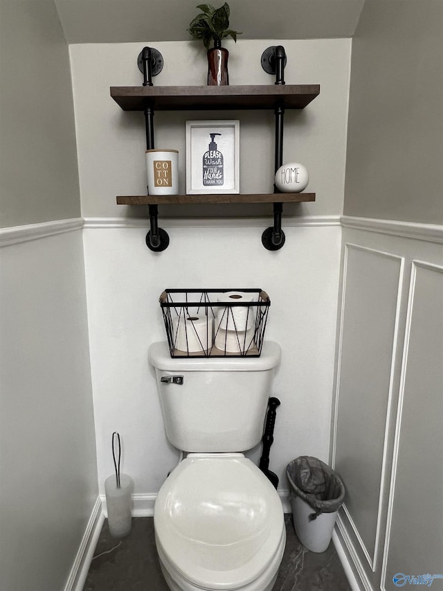 bathroom featuring marble finish floor, a wainscoted wall, a decorative wall, and toilet