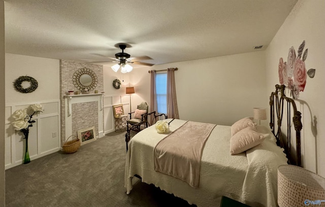 bedroom featuring a textured ceiling, carpet flooring, visible vents, a ceiling fan, and a lit fireplace