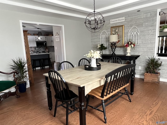 dining space with a tray ceiling, an inviting chandelier, an accent wall, wood finished floors, and baseboards