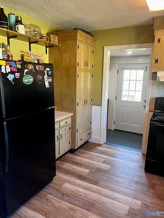 kitchen featuring a textured ceiling, black appliances, exhaust hood, and wood finished floors