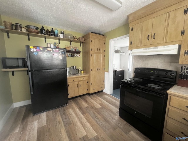 kitchen with backsplash, a textured ceiling, wood finished floors, under cabinet range hood, and black appliances