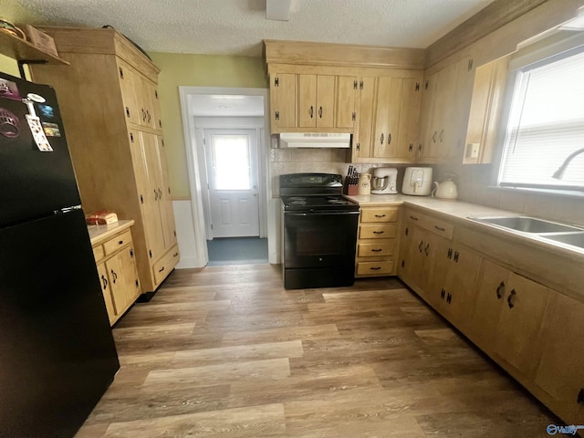 kitchen with under cabinet range hood, a sink, light countertops, light brown cabinetry, and black appliances