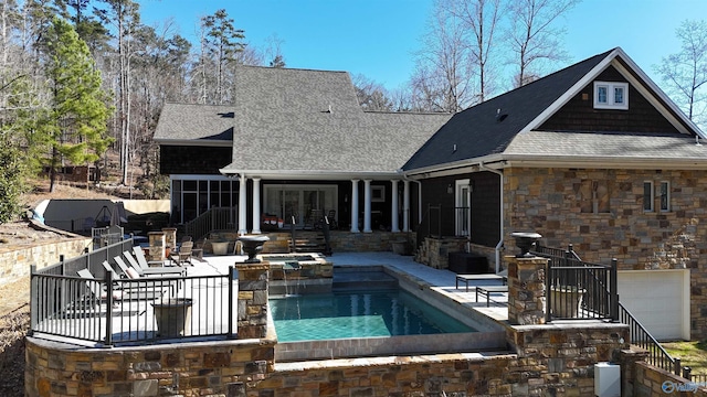 back of house with stone siding, an outdoor pool, a shingled roof, and a patio