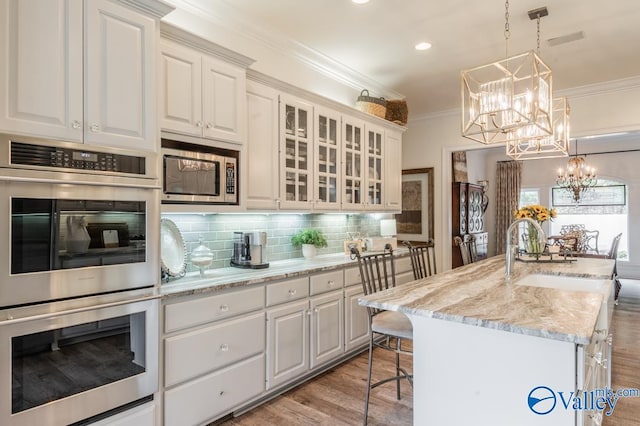 kitchen featuring white cabinetry, stainless steel appliances, pendant lighting, a center island with sink, and light hardwood / wood-style floors