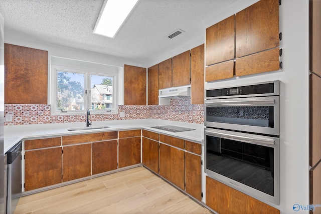 kitchen with under cabinet range hood, appliances with stainless steel finishes, brown cabinetry, and a sink