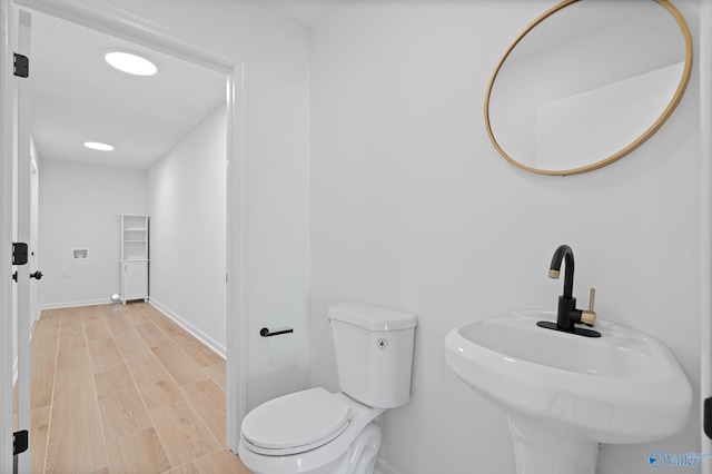 bathroom featuring toilet, wood finished floors, baseboards, and a sink