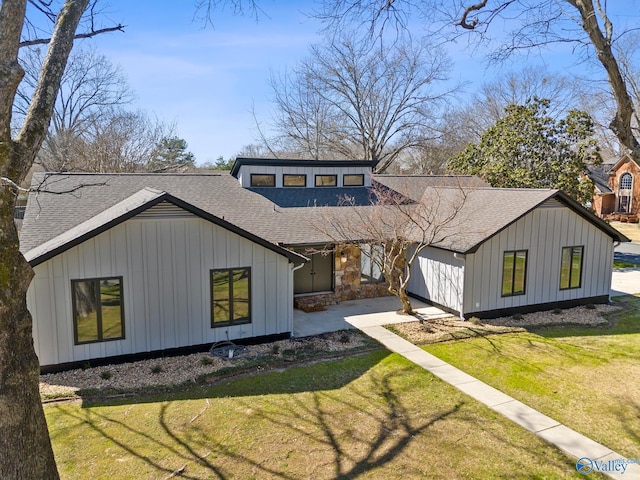 view of front facade with a patio area, board and batten siding, a front yard, and roof with shingles