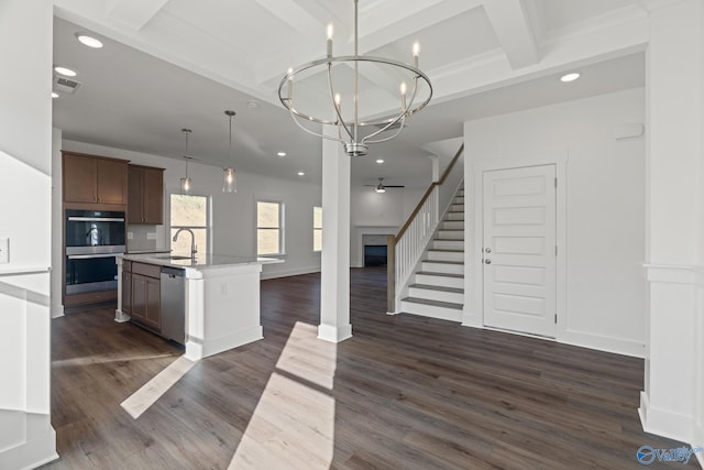 kitchen featuring an island with sink, appliances with stainless steel finishes, ceiling fan with notable chandelier, and dark wood-type flooring