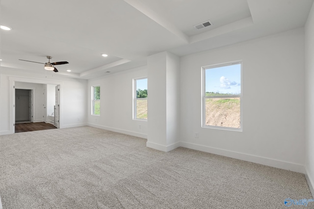 empty room with a raised ceiling, carpet, and ceiling fan