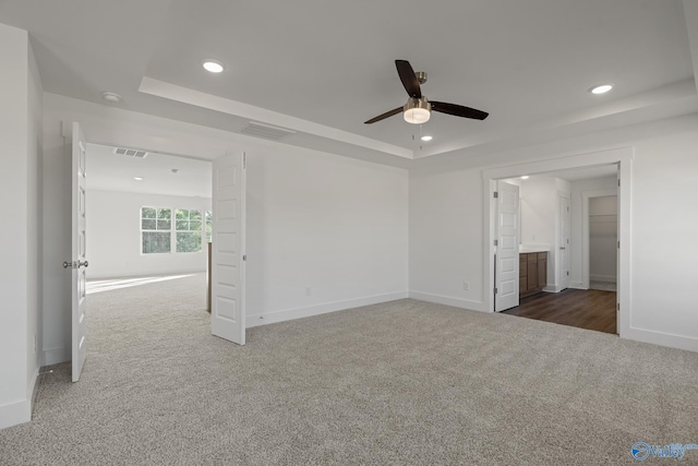 unfurnished bedroom featuring a tray ceiling, dark colored carpet, ceiling fan, and ensuite bath