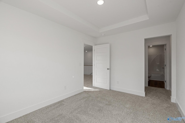 unfurnished bedroom with a raised ceiling and carpet floors