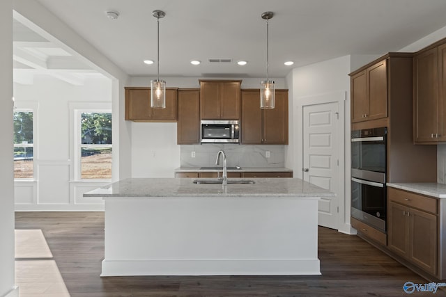 kitchen with a center island with sink, sink, stainless steel appliances, and light stone countertops