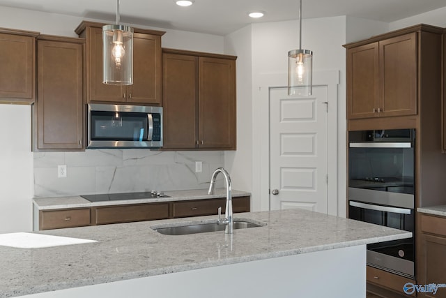 kitchen with light stone counters, pendant lighting, appliances with stainless steel finishes, and decorative backsplash