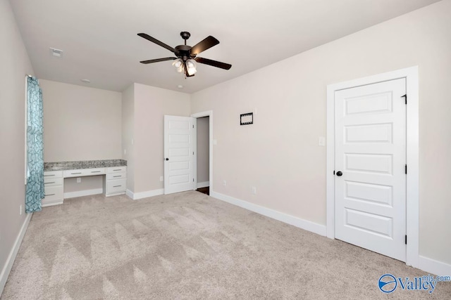 unfurnished bedroom with built in desk, ceiling fan, and light colored carpet