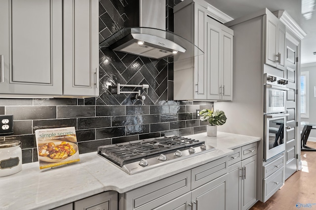 kitchen with hardwood / wood-style floors, wall chimney range hood, light stone countertops, appliances with stainless steel finishes, and tasteful backsplash