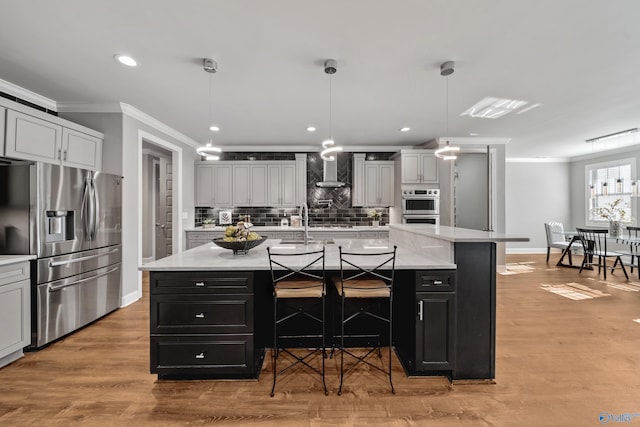 kitchen featuring a kitchen breakfast bar, hanging light fixtures, appliances with stainless steel finishes, a large island, and light hardwood / wood-style floors