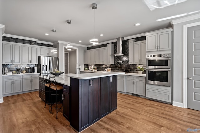 kitchen with pendant lighting, a kitchen island with sink, a kitchen breakfast bar, wall chimney exhaust hood, and stainless steel appliances