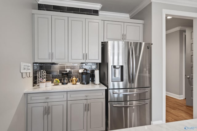 kitchen featuring light stone counters, stainless steel fridge, crown molding, decorative backsplash, and hardwood / wood-style flooring