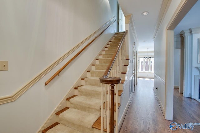 stairway with crown molding, baseboards, decorative columns, an inviting chandelier, and wood finished floors