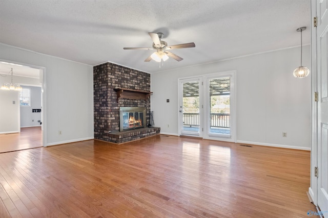 unfurnished living room featuring light hardwood / wood-style flooring, ornamental molding, a brick fireplace, a textured ceiling, and ceiling fan